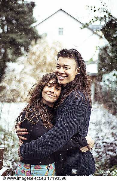 mixed-race queer women couple hug and smile in snow in europe winter