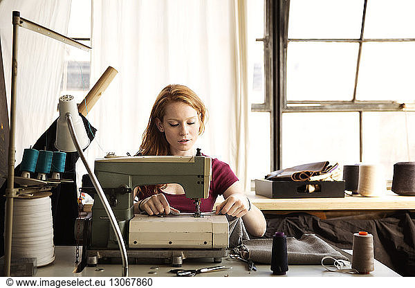 Modedesignerin arbeitet an einer Nähmaschine in einer hell erleuchteten Werkstatt