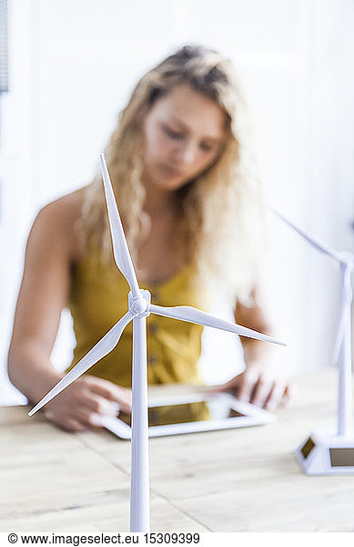Modell einer Windkraftanlage und Frau mit digitalem Tablett im Hintergrund in einem Büro
