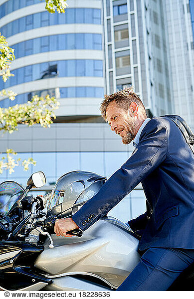 Modern businessman in full suit is sitting on the motorbike outdoors
