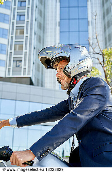 Modern businessman in full suit while sitting on motorbike outdoors