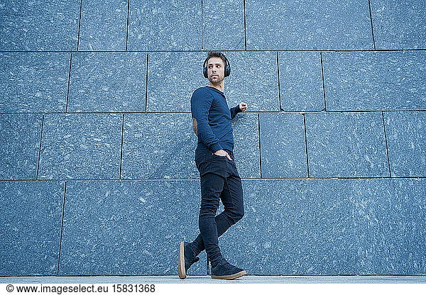 modern man in casual clothes leaning against a wall listening to music