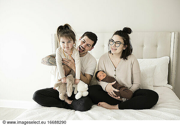 Moderne Millennial-Familie mit Kleinkind und Neugeborenem spielt auf weißem Bett