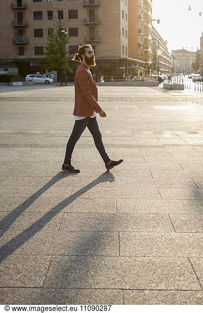 Modischer junger Mann  der auf einem Platz läuft.