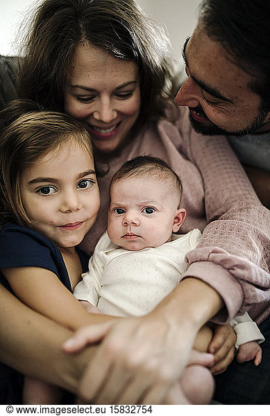 Mom and dad with beard hugging infant and young daughter