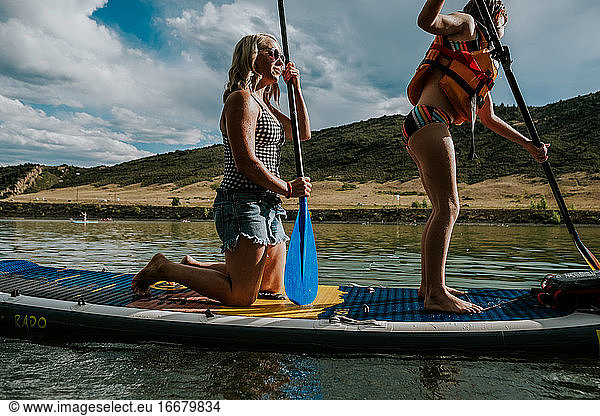 Mom and daughter paddle boarding together on a lake