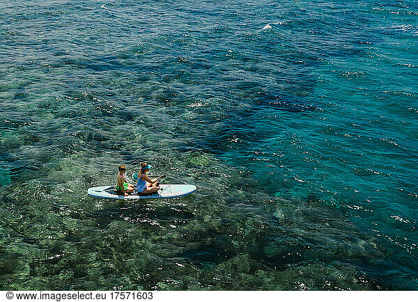 Mom and son stand up paddle boarding over ocean coral reefs