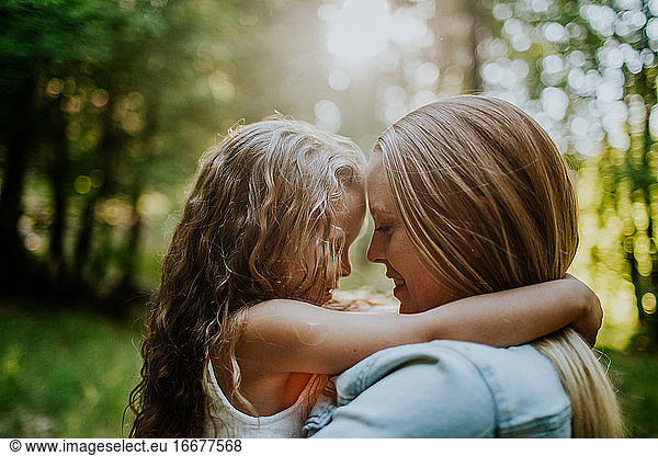 Mom and young daughter hugging smiling in afternoon sun