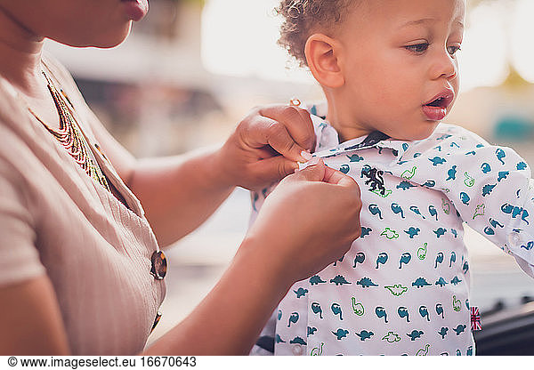 Mom buttoning baby boy's shirt close up to hands and boy's face.