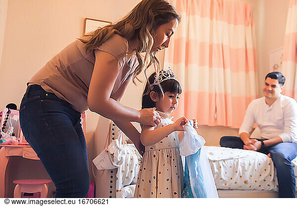 Mom  dad and daughter in bedroom picking out a princess dress for girl