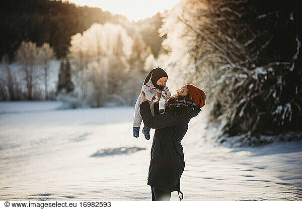 Mom holding baby up in snowy woods during sunset in Norway in winter