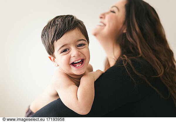 Mom holding toddler while they are both laughing.