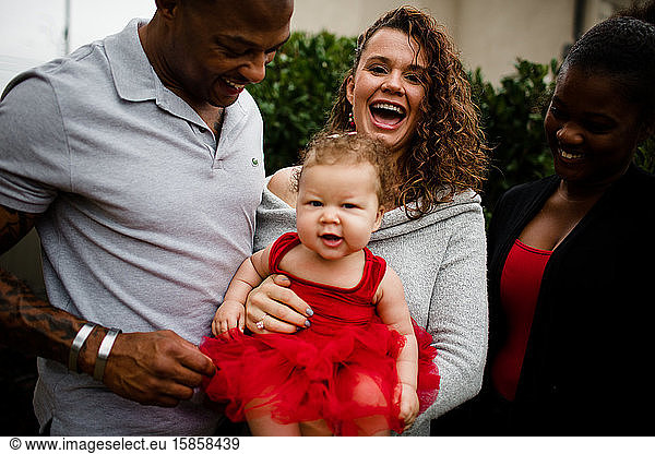 Mom Laughing & Holding Biracial Daughter as Father and Sister Look On