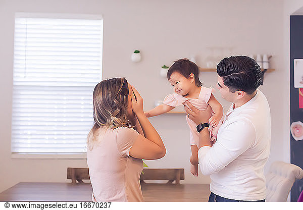 Mom playing peekaboo with baby daughter while dad hold her.