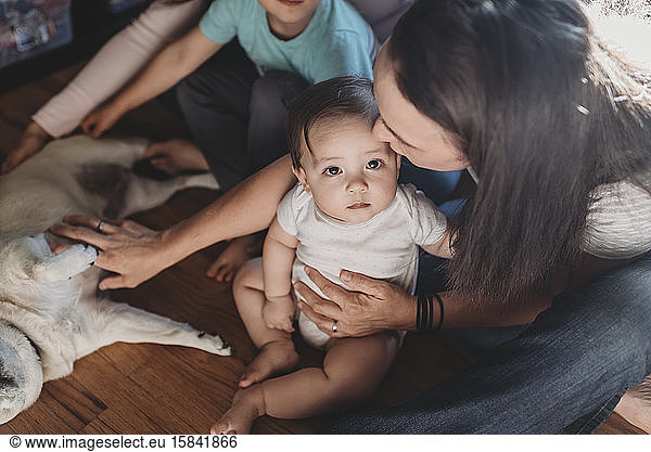 Mom sitting on floor holding baby daughter and petting family Pug