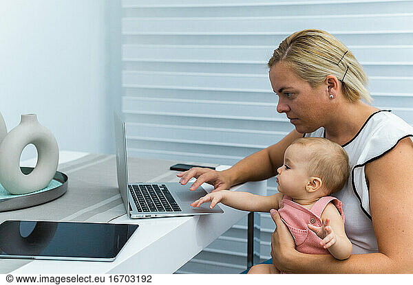 MOM TELEWORKING AND WITH HER BABY IN ARMS