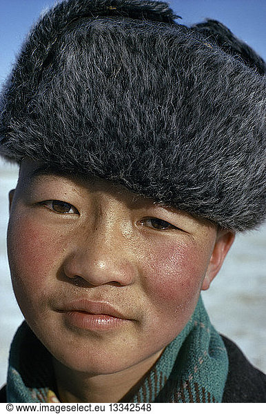 MONGOLIA Children Altai provincial capital. Portrait of young boy with typical fur hat with ear flaps against bitter winter cold.