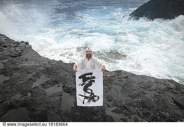 Monk showing calligraphy on paper standing in front of sea