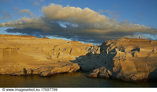 Morgenlicht  blauer Himmel  grau-weiße Wolken  vom Morgenlicht angestrahltes Tuffgestein  2 Menschen auf Tuff-Felsen  Meeresarm  Sarakiniko Beach  Insel Milos  Kykladen  Griechenland  Europa
