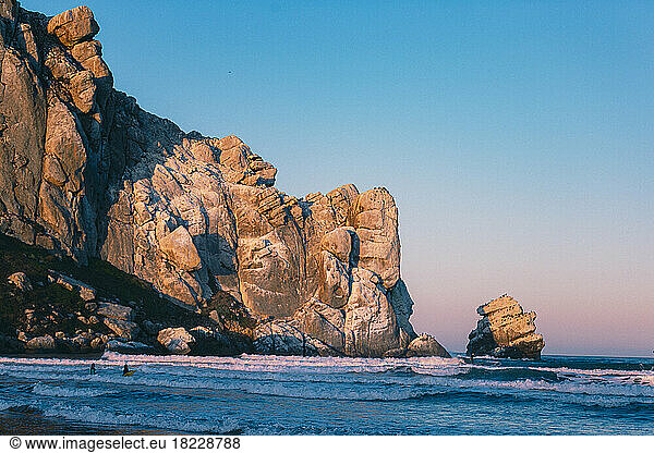 Morning light illuminates a large rock in the ocean.