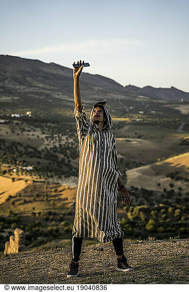 Moroccan man in typical Arabic attire lifting mobile phone up.