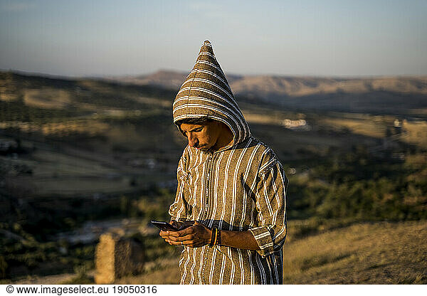 Moroccan man in typical Arabic attire with mobile phone in hand.