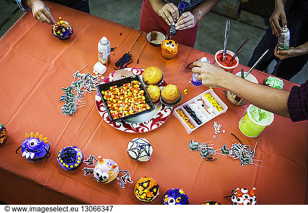 Mother and children decorating muffins at table during Halloween party