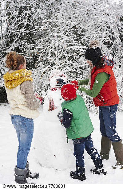 Mother and children making snowman outdoors