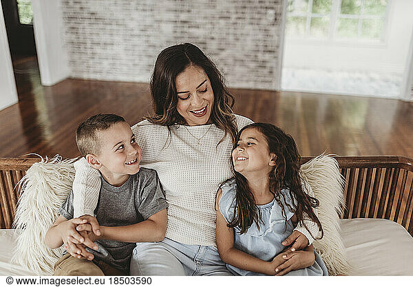 Mother and children smiling at each other while sitting on couch
