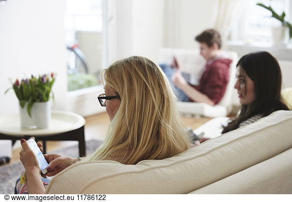 Mother and children using technology while sitting on sofa at home