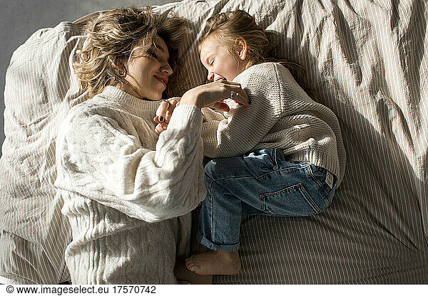 Mother and daugher in similar sweaters lying in bed and playing