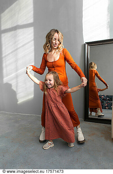 Mother and daugher in similar terracotta dresses dancing at home