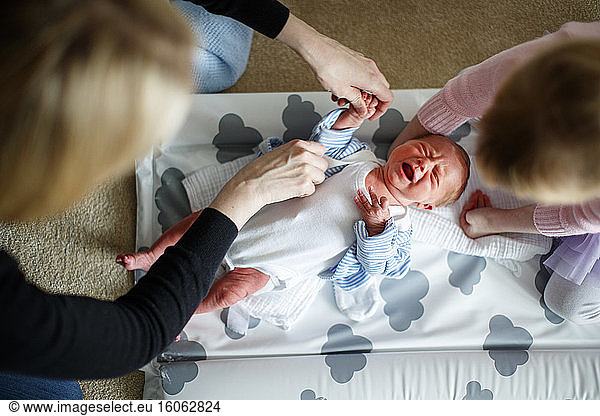 Mother and daugher tending to crying baby on changing mat