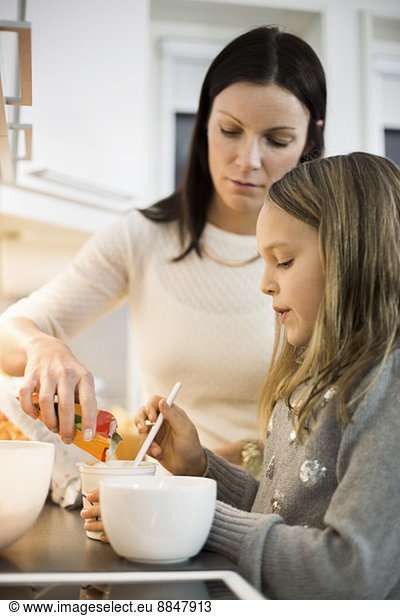 Mother and daughter adding flavor in cup at kitchen
