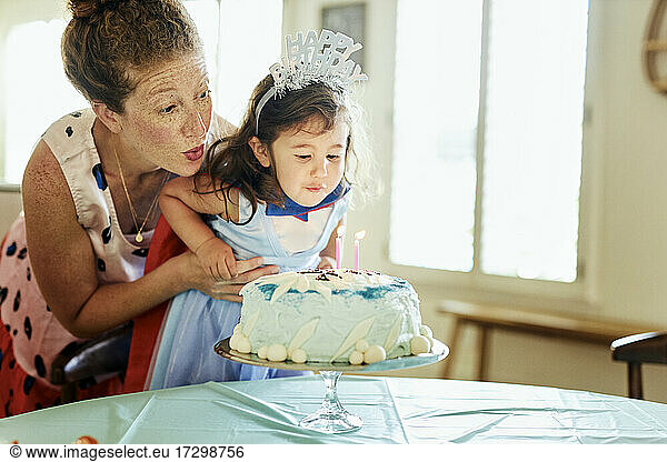 Mother and daughter blowing candles on birthday cake at home