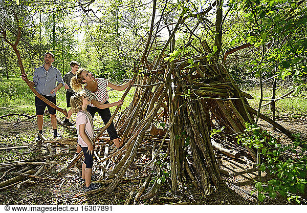 mother and daughter building camp with father and brother collecting log in background at forest