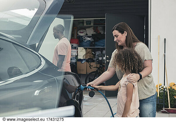 Mother and daughter charging electric car at front yard
