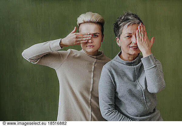 Mother and daughter covering eyes with hand in front of green wall