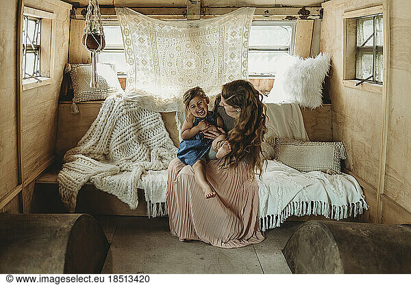 Mother and daughter cuddling and laughing in boho studio setup