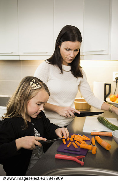 Mother and daughter cutting vegetables in kitchen