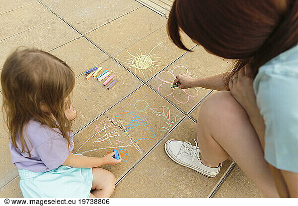 Mother and daughter drawing on tiled floor at park