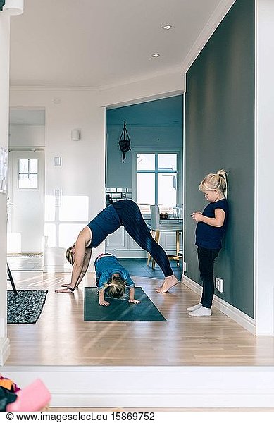 Mother and daughter exercising on mat while girl standing in living room at home