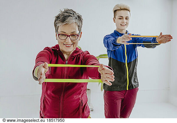 Mother and daughter exercising with resistance bands in front of white wall