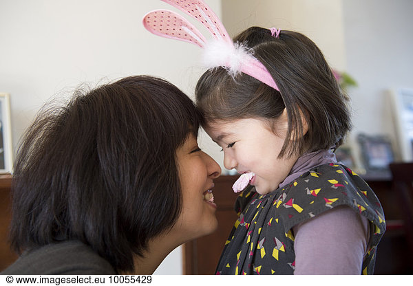 Mother and daughter  face to face  daughter wearing bunny ears and holding sweet in her mouth