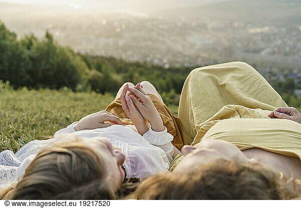 Mother and daughter holding hands and relaxing at sunset