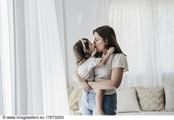Mother and daughter kissing each other at home