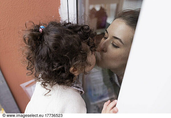 Mother and daughter kissing through window pane
