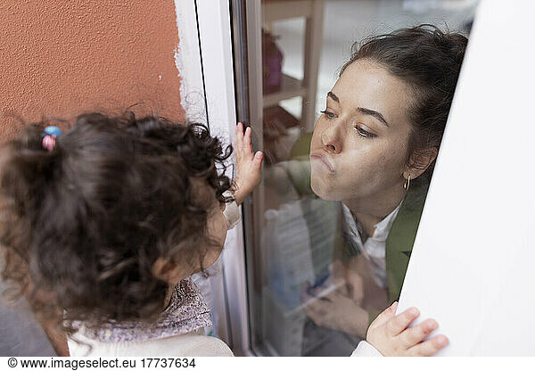 Mother and daughter kissing through window pane
