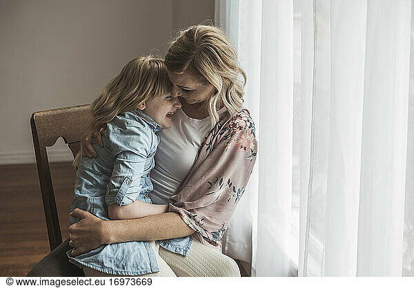 Mother and daughter laughing close together in natural light studio