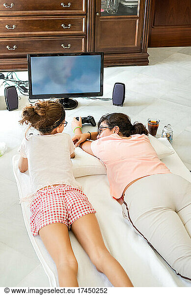 Mother and daughter lying on floor playing video game together at home